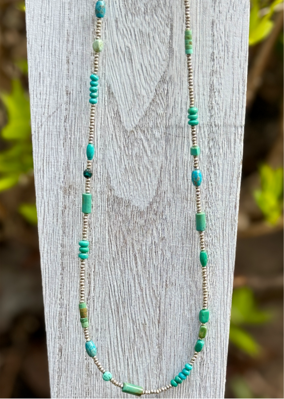 A necklace with varied colors of turquoise beads and fine silver beads displayed on a wooden stand.