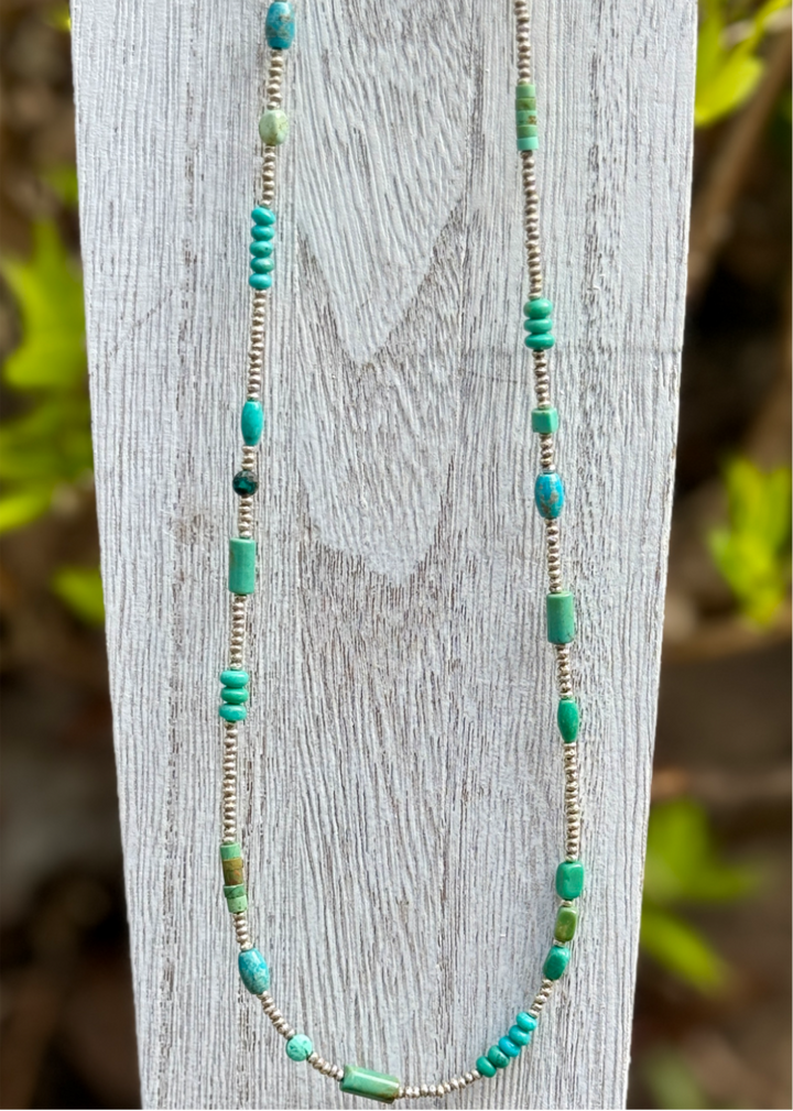 A necklace with varied colors of turquoise beads and fine silver beads displayed on a wooden stand.