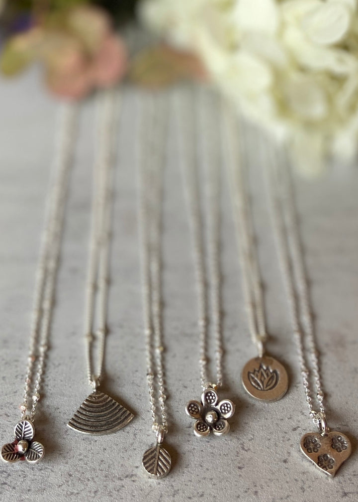 A collection of four silver charm necklaces with different pendants, displayed against a neutral background.