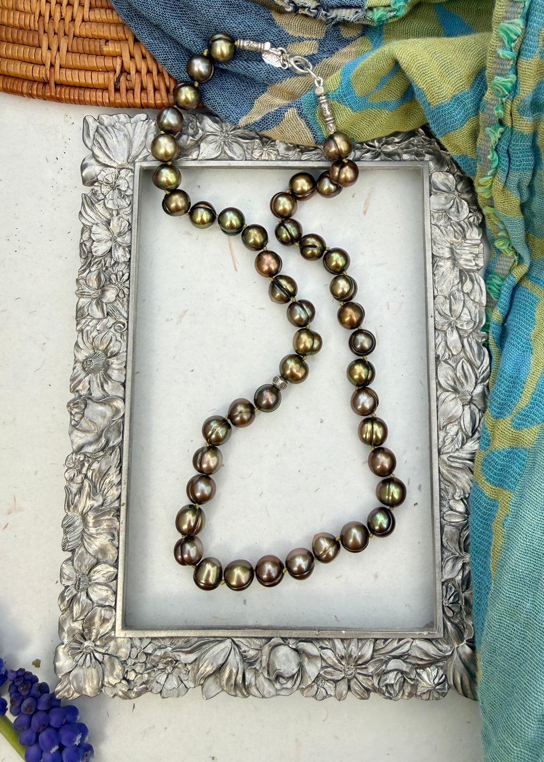 Pearl necklace on a decorative silver frame with a colorful scarf in the background