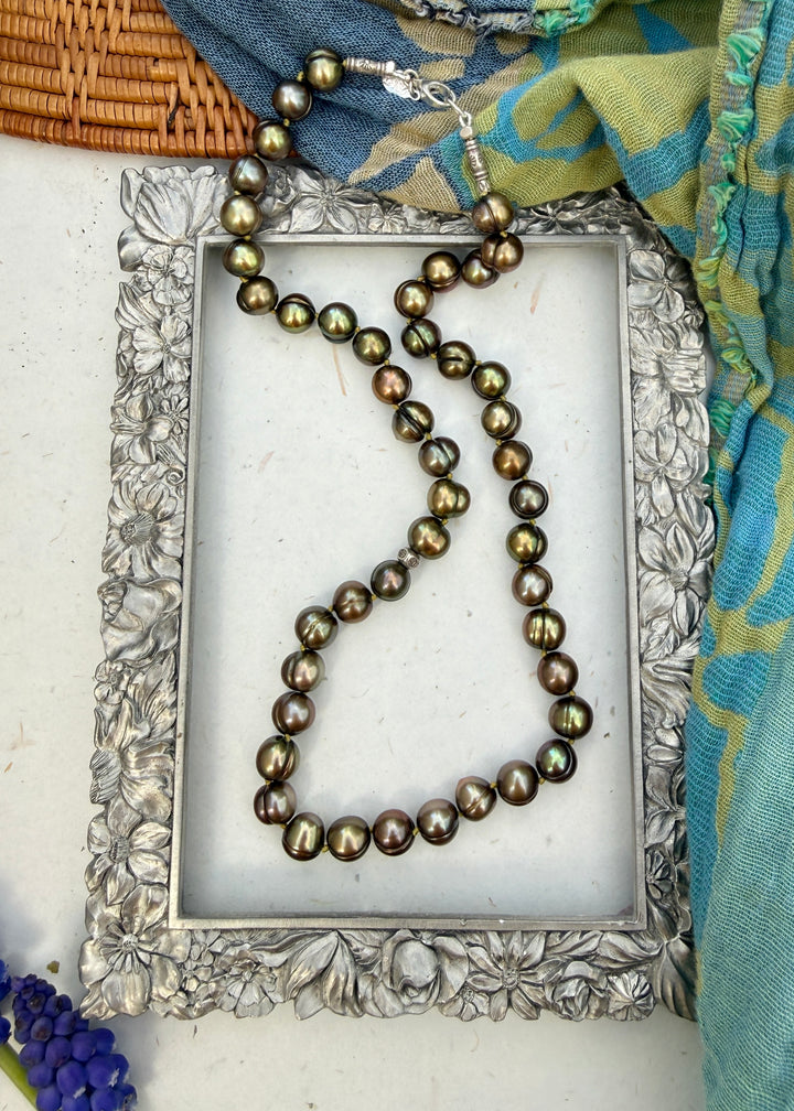 Pearl necklace on a decorative silver frame with a colorful scarf in the background
