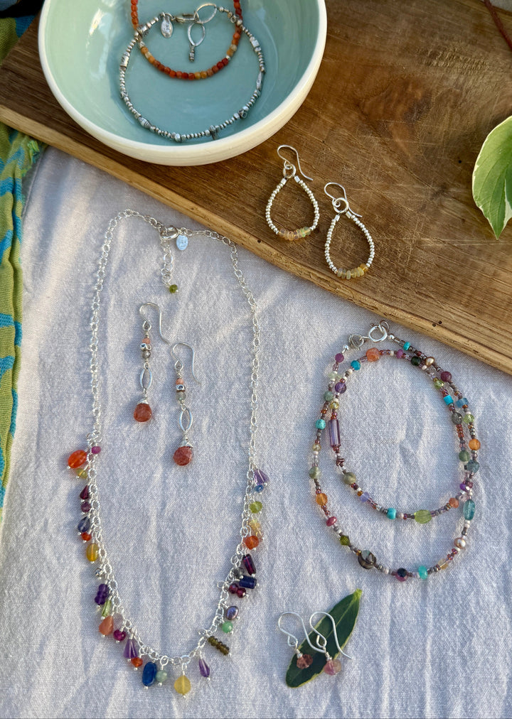 Jewelry including necklaces and earrings displayed on a wooden surface with a bowl containing more jewelry.