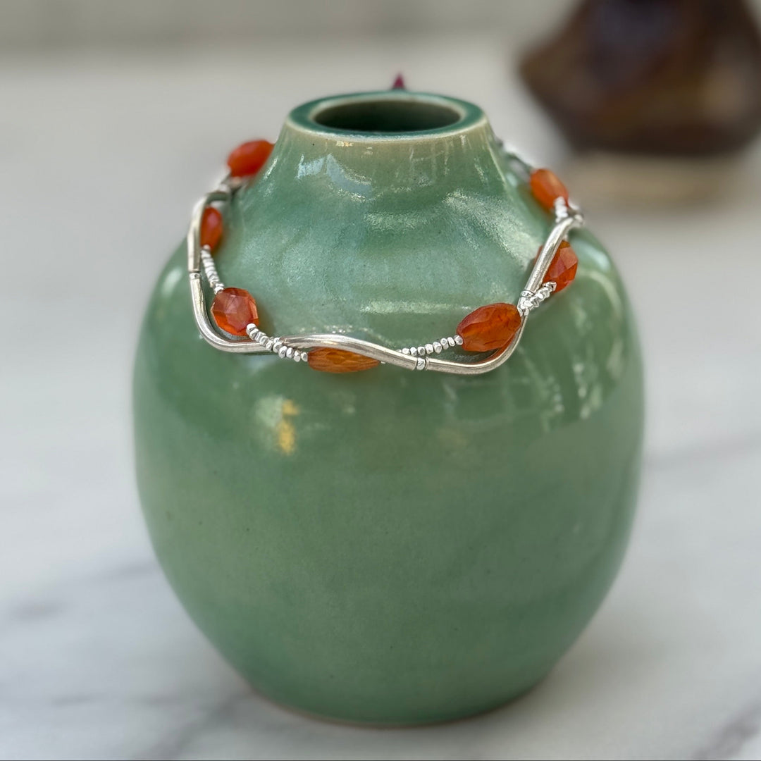 Green ceramic vase with a silver bracelet on a marble surface
